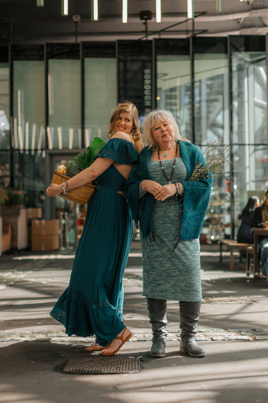 Witchy, ethereal women dressed in teal, explore Borough Market, London. Wearing spiritual jewellery and holding a basket of fruit and veg on market day. 